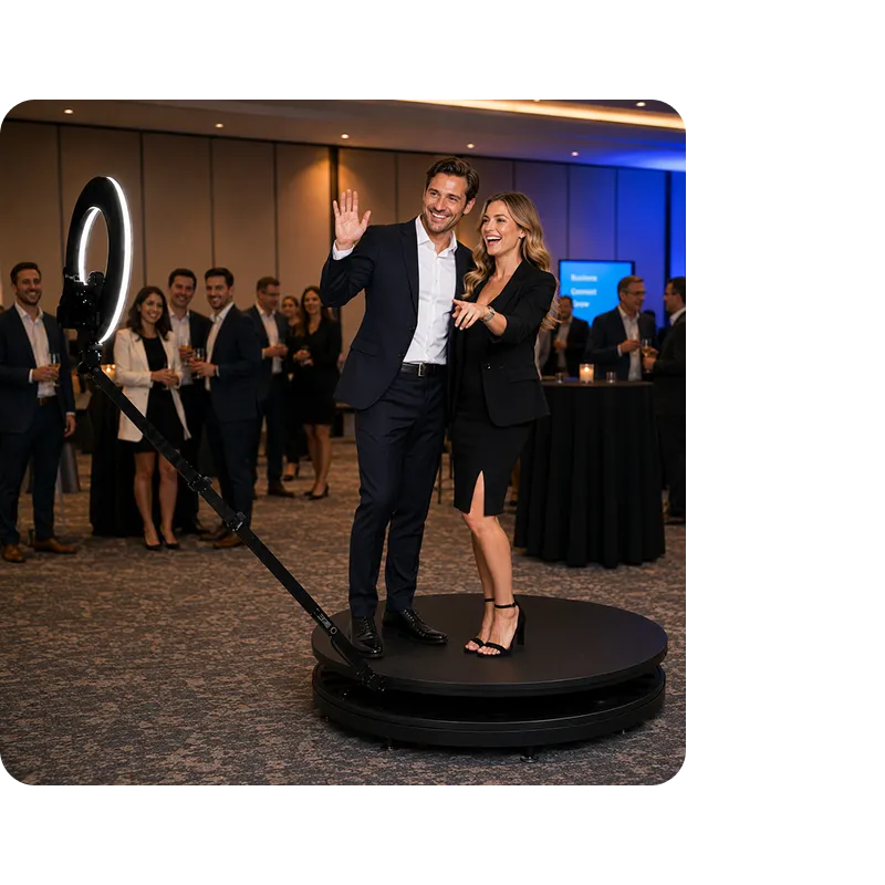 360 Photo Booth at Corporate Gala Man and woman posing on a rotating 360 video booth platform at a corporate gala, surrounded by guests in business attire, with blue and orange ambient lighting in the background.