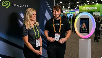 Seagate Tech Conference Photo Booth Demo Two staff members demonstrate an AI photo booth at a tech conference trade show, with Seagate and NVIDIA branding visible in background
