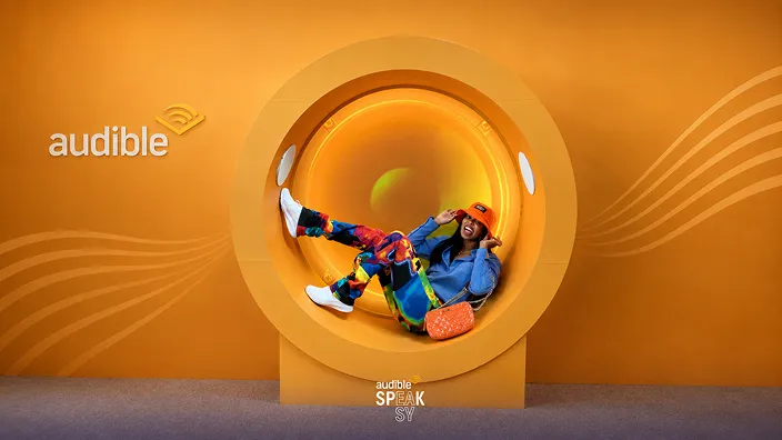 Colorful person inside yellow circular photo booth with Audible branding and orange gradient background