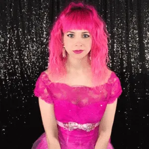 Minimalist Expression for Elegant Boomerangs Woman in pink wig with neutral expression against sequin backdrop