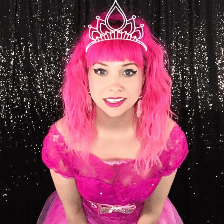 Portrait-Style Boomerang Technique Woman in bright pink wig and tiara wearing a fuchsia sequined dress poses in front of a black sequined backdrop, smiling at camera.