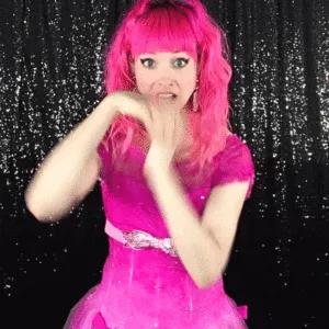 Woman Touching Face in Pink Wig Woman in bright pink wig and dress posing playfully with hands near face against a black sequin backdrop