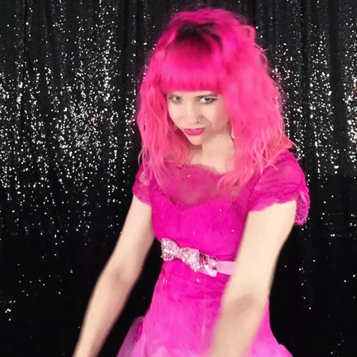 Woman Posing Downward in Pink Costume Woman in bright pink wig and sequined dress posing against black sequin backdrop for boomerang video