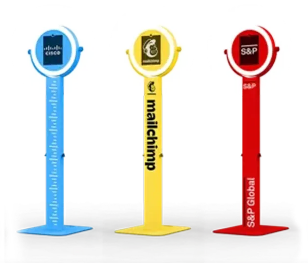 Three branded photo booth kiosks in blue, yellow, and red showing Cisco, Mailchimp, and S&P Global logos