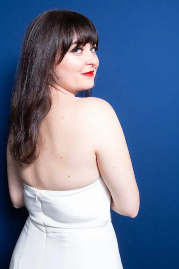 Woman in white strapless gown looking over shoulder against blue backdrop