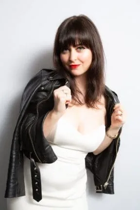 Woman in white dress with black leather jacket against neutral backdrop