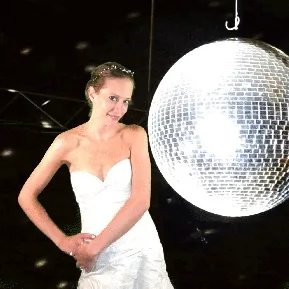 Disco Ball Wedding Photo Bride in white strapless dress posing beside oversized illuminated disco ball against black background with confetti