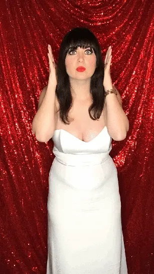 Woman in white dress with playful expression against red sequin backdrop