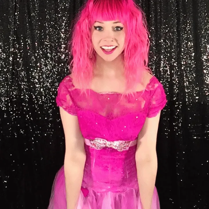 Woman in Pink Dress with Ruffled Neckline Woman in bright pink sequined dress and matching wig smiling at camera against glittering black backdrop, demonstrating vibrant color for boomerang videos.