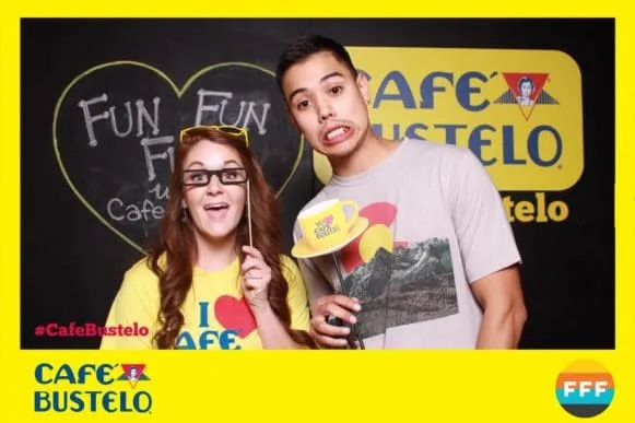 Two guests at Café Bustelo branded photo booth activation holding custom props and smiling at camera with yellow and black branded backdrop