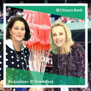 Two women smiling at Citizens Bank trade show booth with Red Sox signage and white feather props