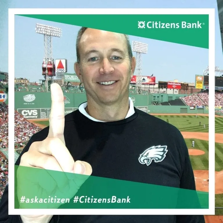 Man in black Eagles shirt giving thumbs up at Citizens Bank-branded photo booth with Fenway Park background