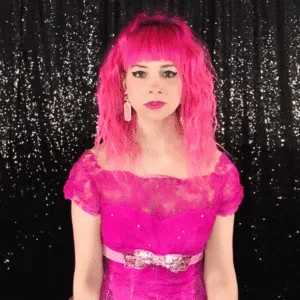Subtle Expression Changes for Boomerang Loops Woman with bright pink wavy wig and matching off-shoulder dress with sequin belt posing against black sparkly backdrop