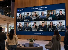 Employee All-Hands Photo Wall — Corporate Implementation Large digital display showing a grid of professional headshots labeled 'Global All-Hands Photo Wall' at a corporate event, with attendees viewing the screen in a modern venue