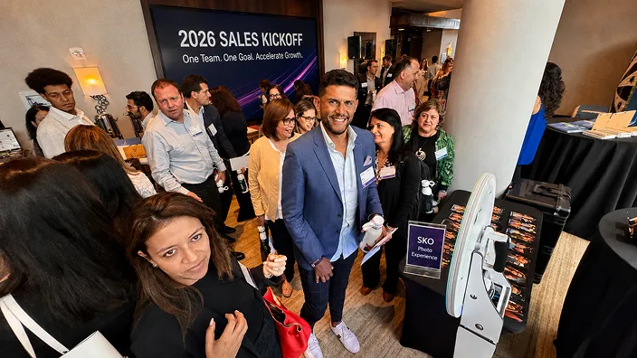 Guests mingling at a 2026 sales kickoff corporate event with an AI photo booth kiosk visible on the right side of the room.