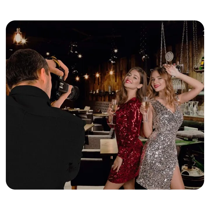 Photographer shooting two women in sequin dresses holding champagne at a rustic bar venue