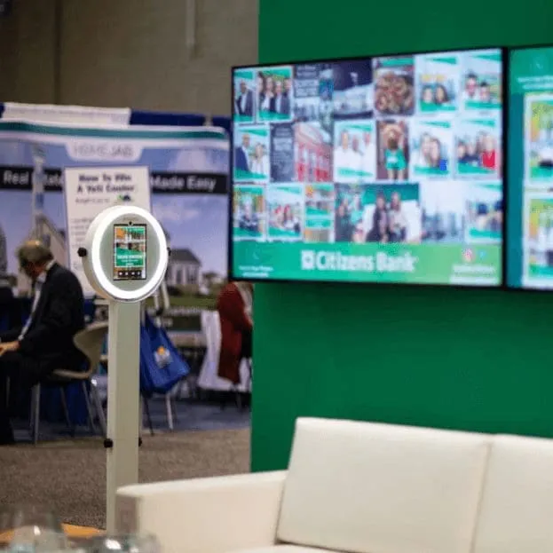 Interactive Photo Display Booth With Ring Lighting FotoRover photo booth with ring light display at trade show, showing live gallery on digital screens behind it
