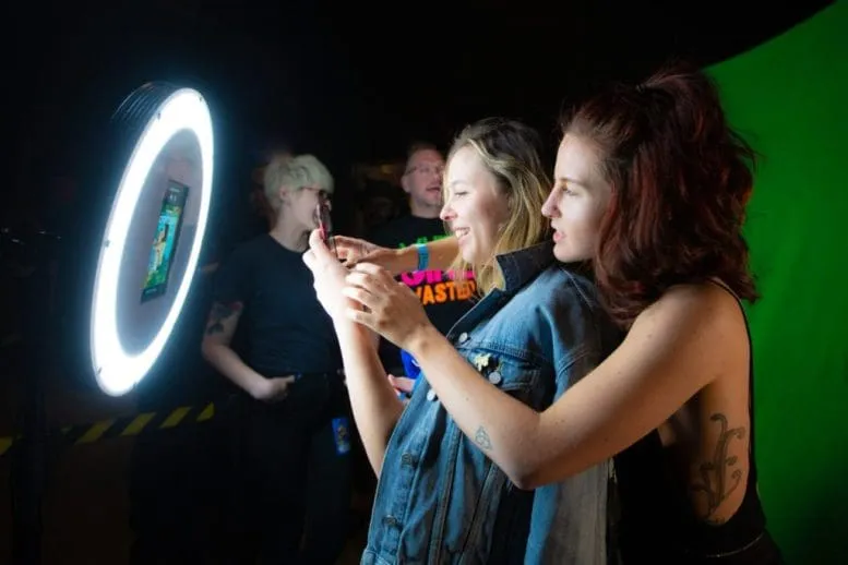 Friends Enjoying FutureFoto Photo Booth Experience Two young women smiling and posing together at illuminated circular photo booth with green screen