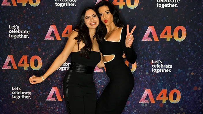 Corporate event brand activation photo Two women posing at an A40 brand activation event with a dark blue backdrop featuring the A40 logo and 'Let's celebrate together' text