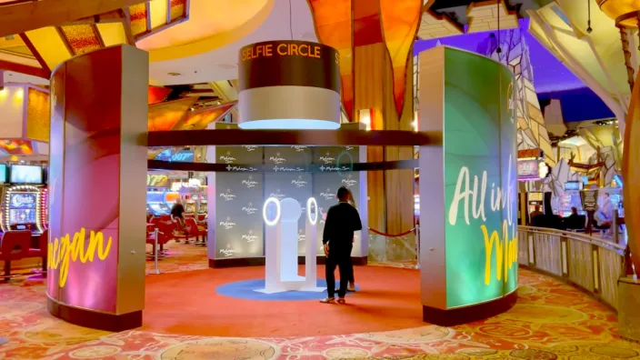 Casino Venue Photo Experience FutureFoto open-air photo booth with illuminated ring light at Mohegan Sun casino, featuring vibrant pink and green branded columns in a spacious venue corridor.