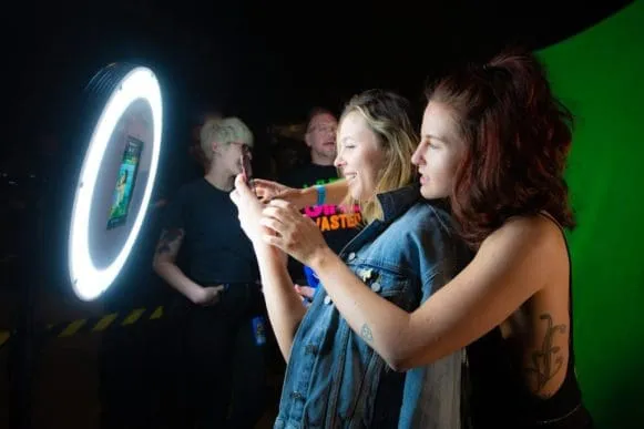 Young people posing playfully with circular neon photo booth frame at night