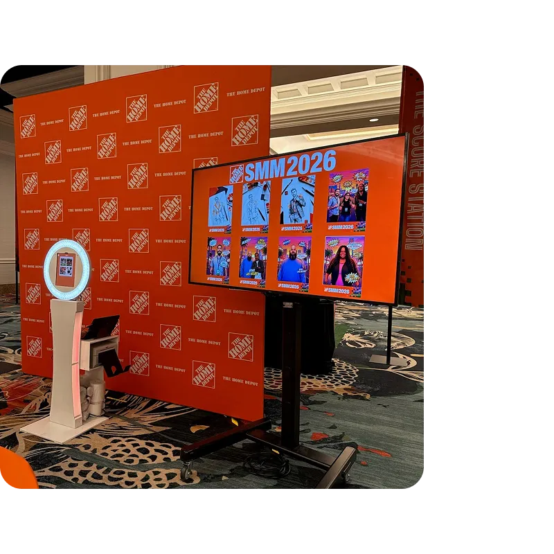 Branded Booth Photo Display Setup FutureFoto open-air photo booth with white kiosk and orange backdrop branded with Home Depot logos and SMIM2026 signage at trade show