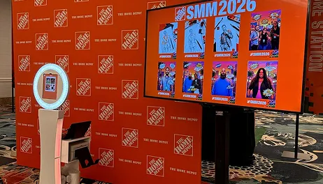 Photo Booth Setup at Brand Event with Display Screen FutureFoto open-air photo booth with white frame beside large orange display screen showing SMM2026 event photos at trade show