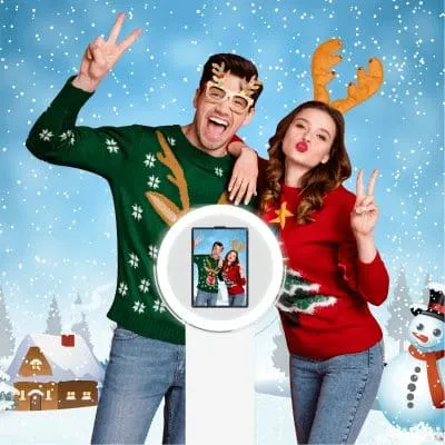 Celebratory couple in holiday sweaters posing in snowy scene with instant photo display