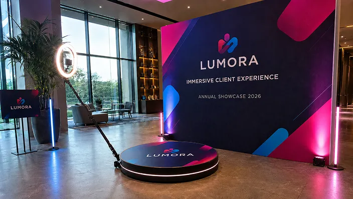 Corporate Branded 360 Booth LUMORA 360 photo booth with spinning platform and ring light at corporate showcase event, branded display wall behind