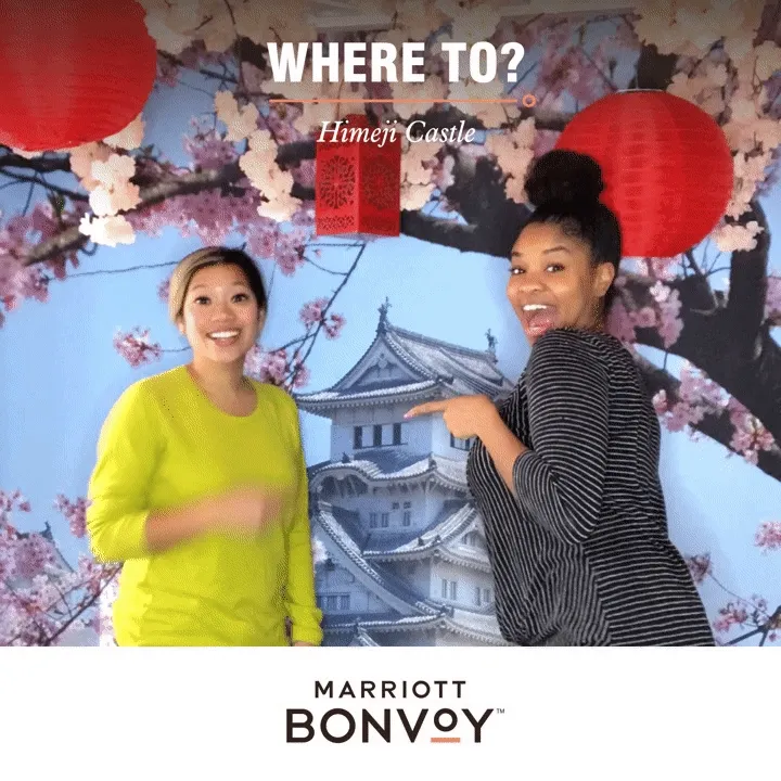 Marriott Bonvoy Himeji Castle Photo Experience Two women posing in front of Himeji Castle backdrop with cherry blossoms and red lanterns at OutSnapped photo booth, Marriott Bonvoy branding below