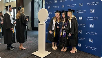 Graduates in caps and gowns using white circular mirror photo booth at Northwood University ceremony