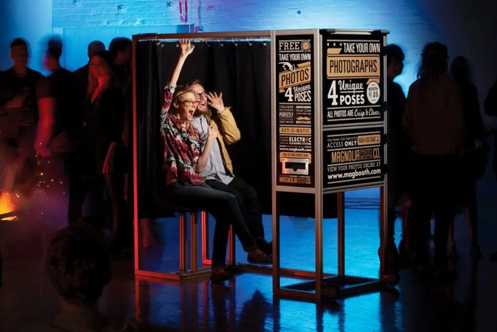 FutureFoto open-air photo booth at event with guests taking photos, illuminated by blue and red lighting against brick wall backdrop