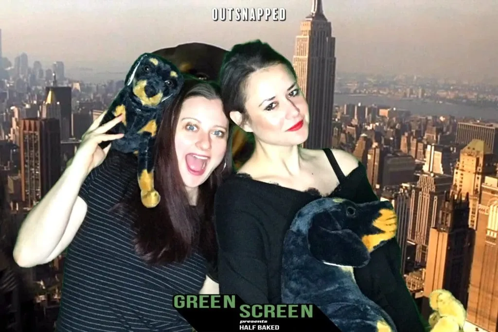 NYC Green Screen Event Photo Two women posing playfully in front of a New York City skyline green screen backdrop at OutSnapped's photo booth, with Empire State Building visible behind them.