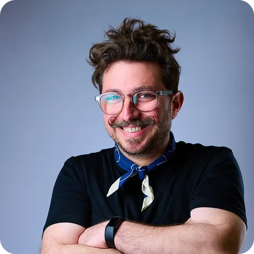OutSnapped Team Member Portrait OutSnapped team member with dark wavy hair, glasses, and blue scarf, smiling at camera with arms crossed