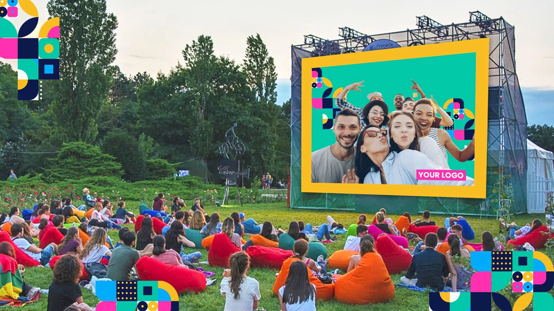 Outdoor event crowd sitting on colorful bean bags watching large screen displaying photo booth photos with yellow and green frame, mountains in background
