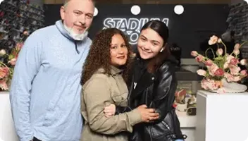 Three guests smiling at an OutSnapped photo booth during a retail activation event, with decorated backdrop and floral arrangements visible behind them.