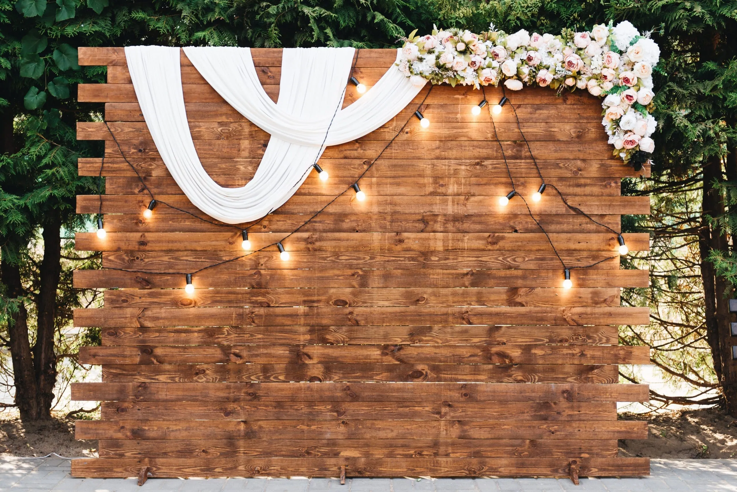 Rustic Wooden Photo Booth Backdrop with Flowers Rustic wood backdrop with white fabric draping, string lights, and floral garland
