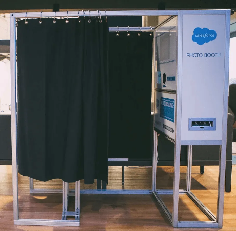 Professional MagBooth Photo Booth Setup Open-air photo booth with dark green curtain backdrop, silver aluminum frame, and Salesforce-branded control panel at a corporate event