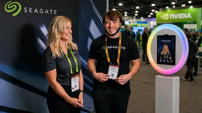Seagate FutureFoto Trade Show Experience Seagate trade show attendees standing beside an OutSnapped FutureFoto interactive photo booth