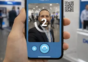 Hand holding smartphone displaying SnapShift AI photo booth interface with guest portrait preview and QR code access button