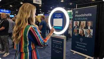 AI Headshots Trade Show Booth Experience Woman with long blonde hair using an AI photo booth with glowing ring light at a trade show, with headshot gallery display visible behind her.