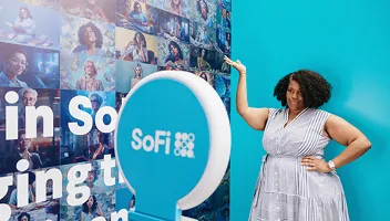 Woman posing next to SoFi-branded photo booth activation with turquoise backdrop and large circular booth logo