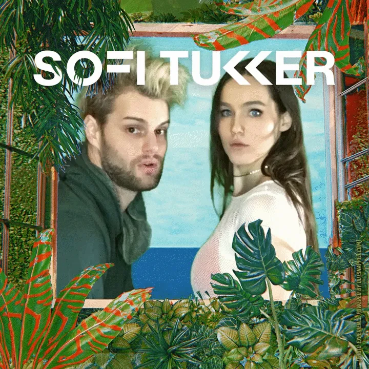 Photo Booth Backdrop with Tropical Florals Two people pose in an OutSnapped photo booth with tropical leaf backdrop and blue ocean scenery, framed by decorative palm fronds and colorful geometric patterns.