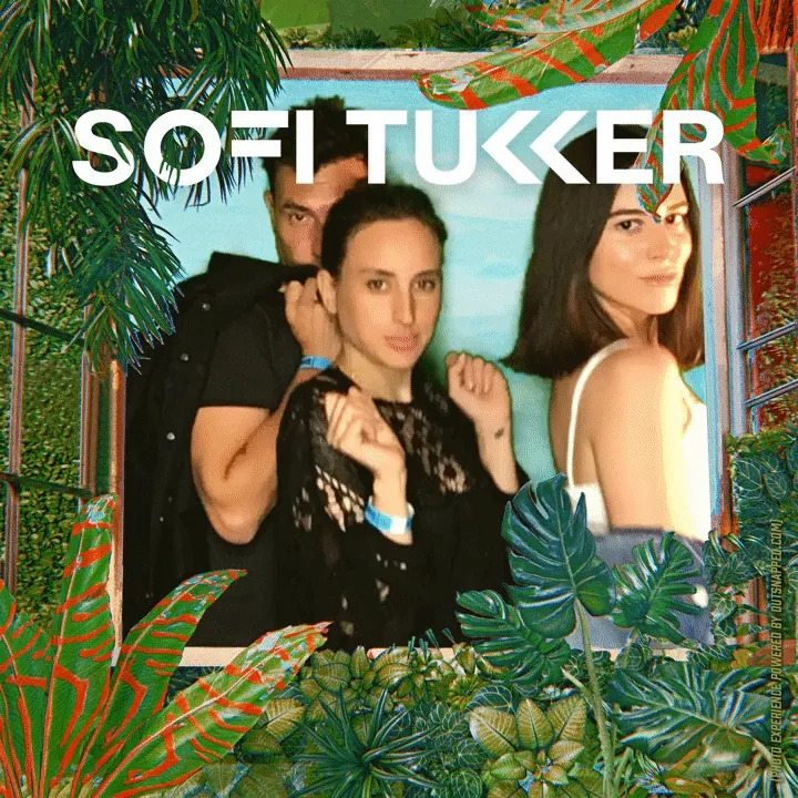 Group Moment at Sofi Tukker Photo Booth Three people posing in OutSnapped photo booth with tropical foliage frame, palm leaves and colorful geometric patterns surrounding them