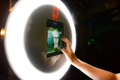 Branded album photo booth experience activation Guest interacting with FutureFoto open-air photo booth at Sofi Tukker's Treehouse Tour, hand reaching toward illuminated ring light display