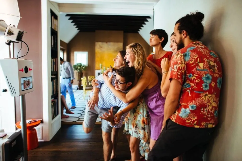 Photo Booth Experience at Event Venue Group of five guests interacting with a touchless photo booth at an indoor event, with the booth's interface visible on the left wall