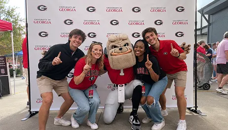 College Campus Photo Booth – Student Event Experience Four people posing with University of Georgia mascot Uga at outdoor event with branded step-and-repeat backdrop
