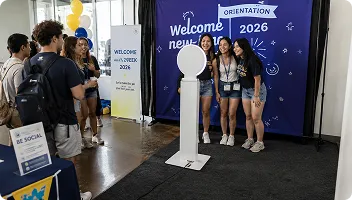 Students posing at OutSnapped mirror booth during university orientation 2026 event, with welcome signage and staff nearby