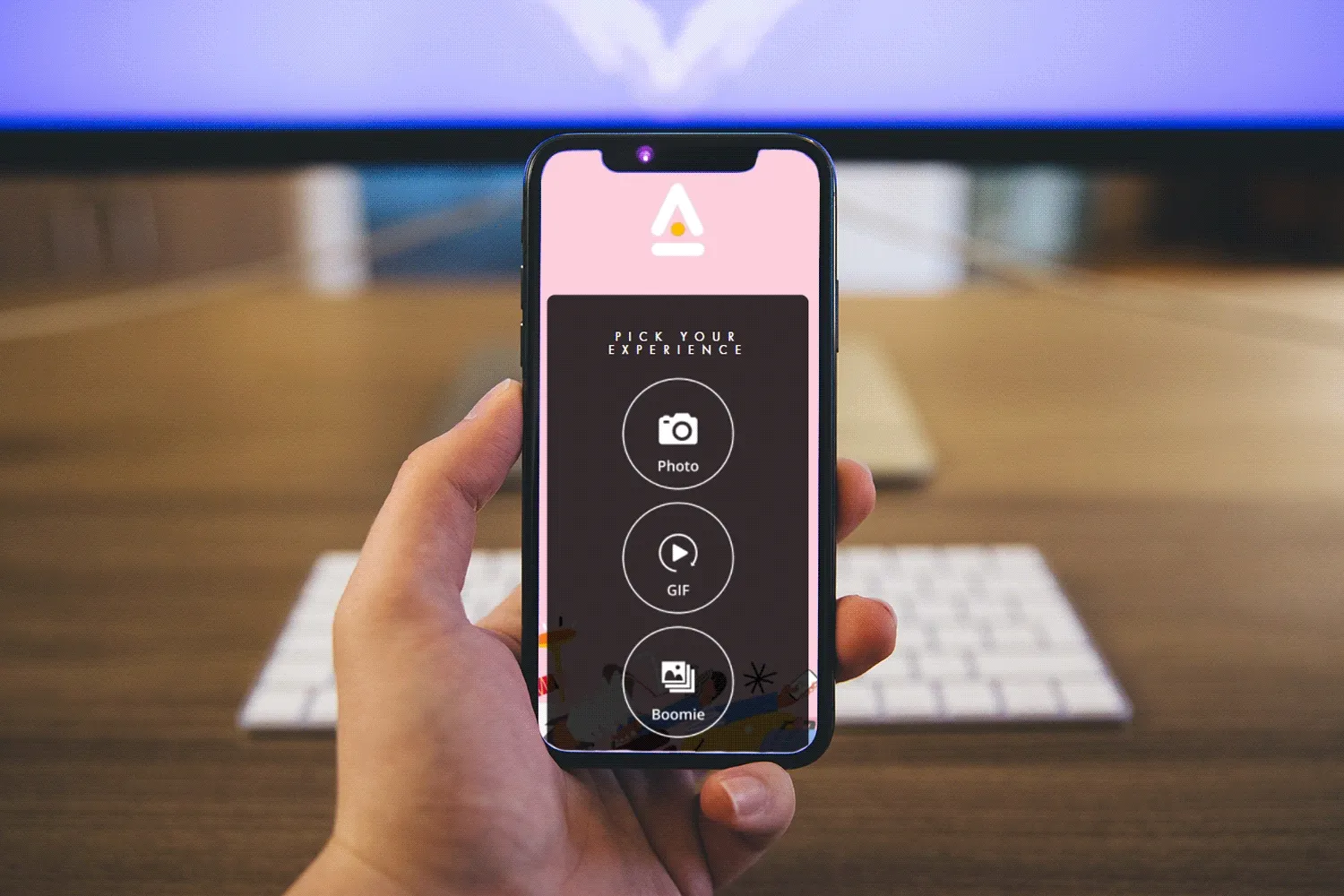 Hand holding smartphone displaying virtual photo booth app interface with Photo, GIF, and Boomerang options on dark screen