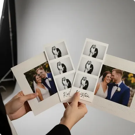 Premium Wedding Photo Booth Prints Hands holding printed photo booth strips from a wedding, featuring black-and-white instant photos and color couple portraits on white cardstock